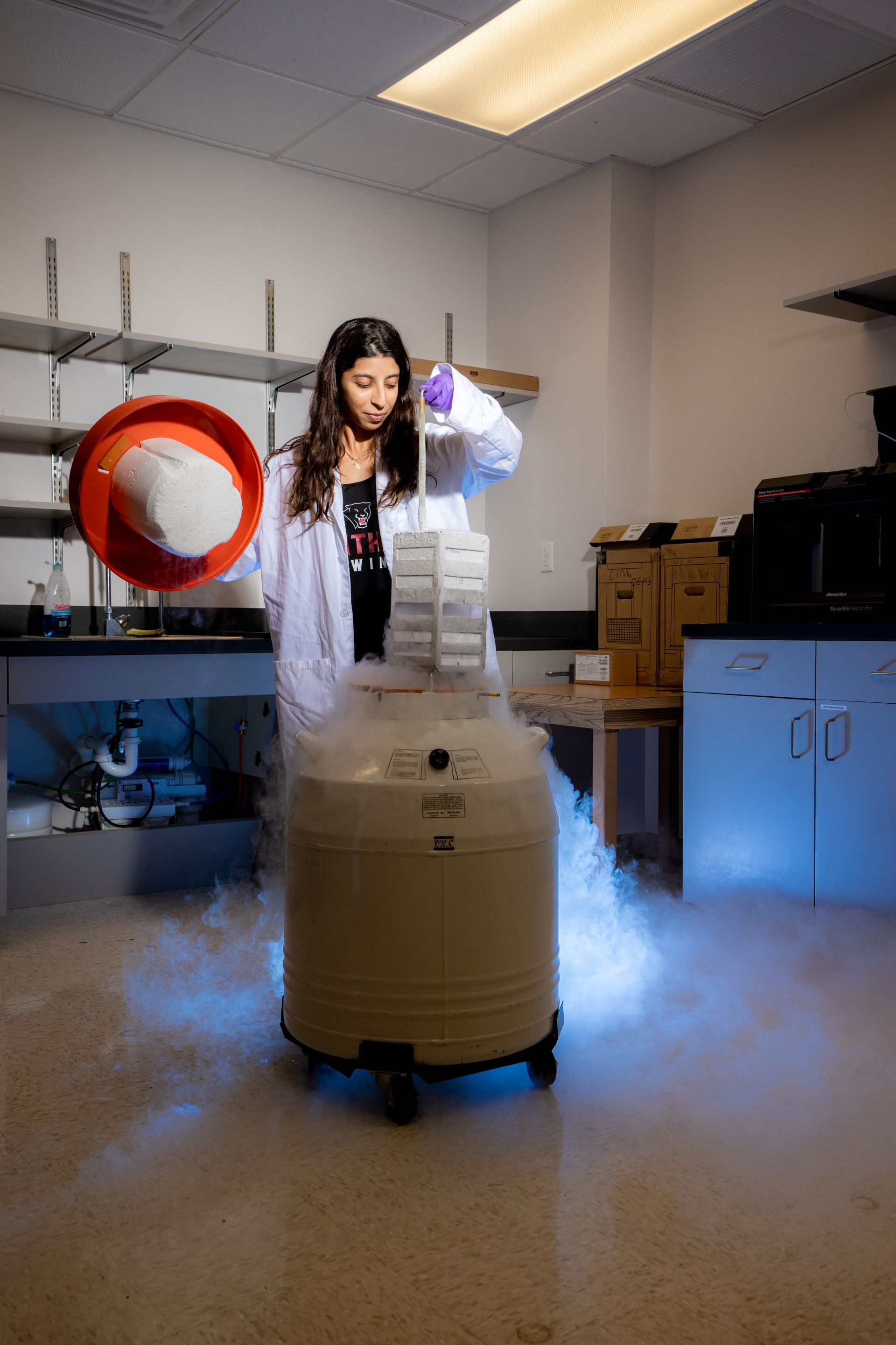 Female scientist in a lab coat pouring liquid nitrogen from a large container, creating a dramatic vapor cloud in a laboratory setting